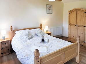 A wooden bed with floral bedding, a bedside lamp, a nightstand, a radiator, and a wooden wardrobe.