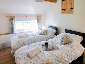 A double bed with floral bedding, a tray with a candle and two cups, and a window with curtains.