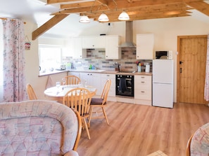A kitchen with wooden beams, white cabinets, a dining table with chairs, and a refrigerator.