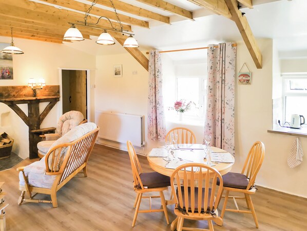 A cozy room with a wooden ceiling, a dining table with chairs, a radiator, and a window with curtains.
