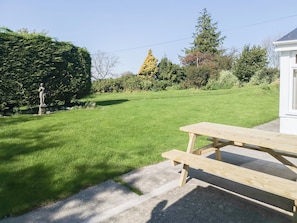 A grassy outdoor area with a wooden picnic table and a stone statue.