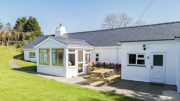 A white house with a conservatory, a wooden table, and a garden. - 2 bedroom accommodation in Carmel, near Caernarfon (Carmel, near Caernarfon)