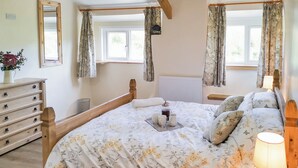 A bedroom with a wooden bed frame, floral bedding, a bedside table with a lamp, a dresser, and a window with curtains. - 2 bedroom accommodation in Carmel, near Caernarfon (Carmel, near Caernarfon)