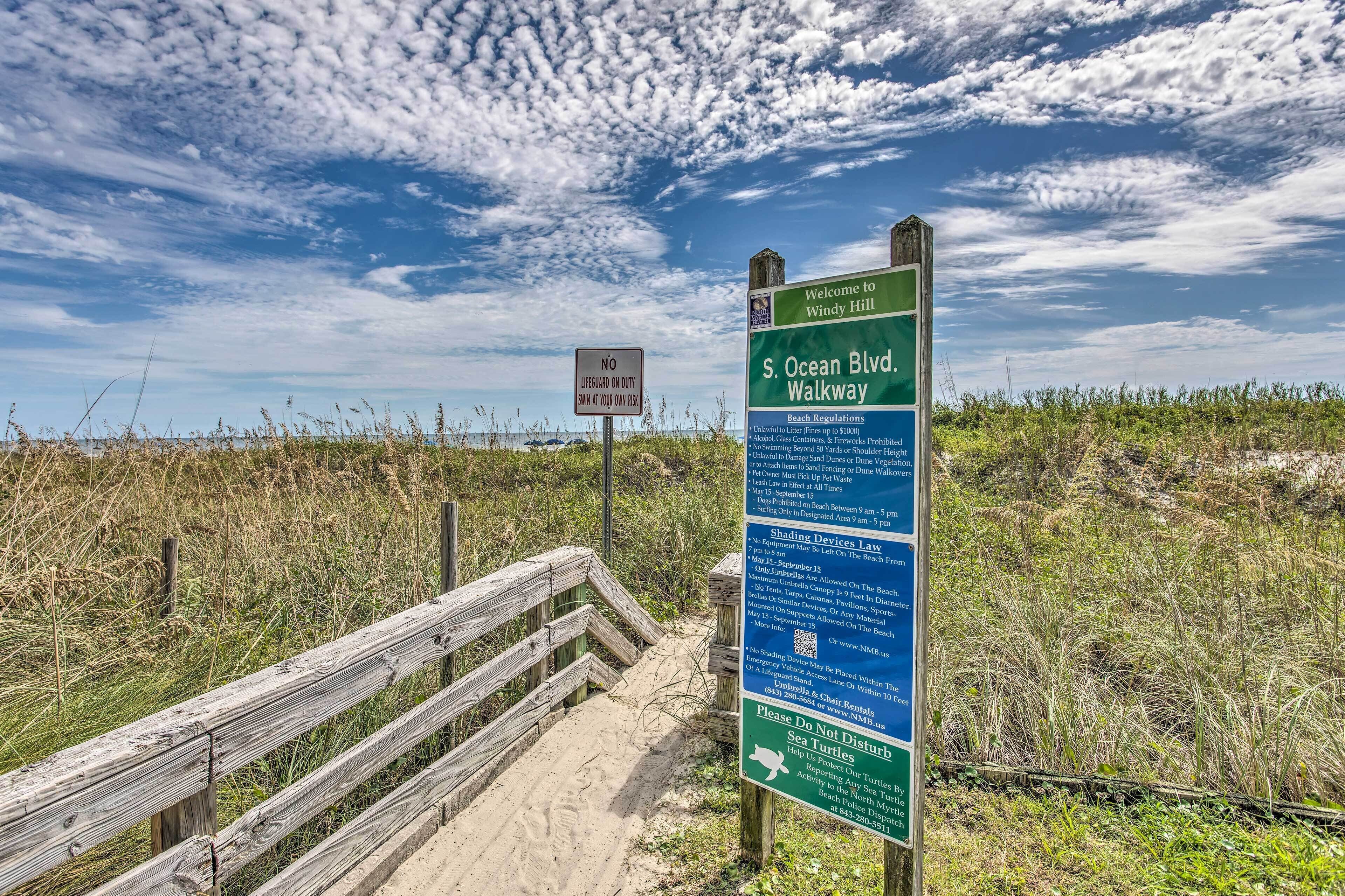 A wooden boardwalk leading to S. Ocean Blvd. Walkway with informational signs about beach regulations and no lifeguard on duty.