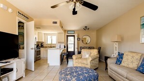 A modern living room with a TV, sofa, ottoman, and a ceiling fan.