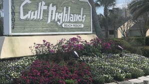 A sign for Gulf Highlands Beach Resort with a landscaped garden in front.