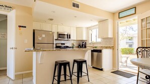 A kitchen with a refrigerator, microwave, and dishwasher. There are two stools and a table with chairs.