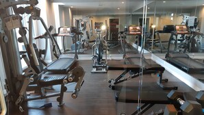 Ein Fitnessstudio mit verschiedenen Trainingsgeräten, einer Spiegelwand und einem Holzboden.
