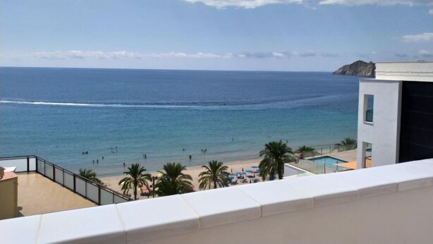 A beach view from a balcony with a pool and palm trees.