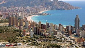 A coastal cityscape with high-rise buildings, a beach, and mountains in the background.