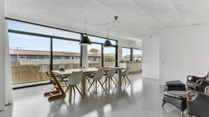 Ruime kamer met een grote eettafel, moderne stoelen en uitzicht op een woonwijk door grote ramen.