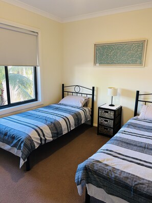 A bedroom with two single beds, a window with blinds, a bedside lamp, and a framed artwork on the wall.