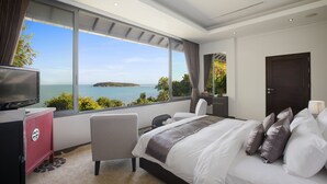 Quarto com uma janela grande, uma cama, uma televisão e uma escrivaninha.