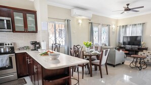 Una cocina moderna con una isla central, comedor con sillas, un sofá y un televisor en la sala.