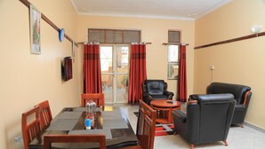 A dining area with a table set for four, a black leather sofa, and a chair. - Apt - Sleeps 4 - Pets Ok - Parking - Garden (Kampala)