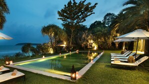 A poolside area with lounge chairs and umbrellas, surrounded by tropical vegetation and a view of the ocean. - Sangsuri Villa 2 (Koh Samui)