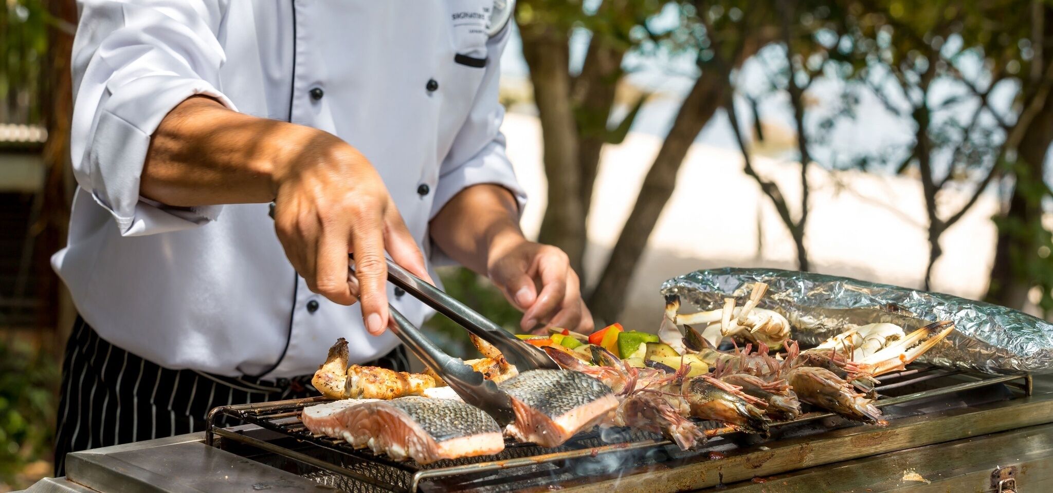 A chef grilling various seafood items outdoors.