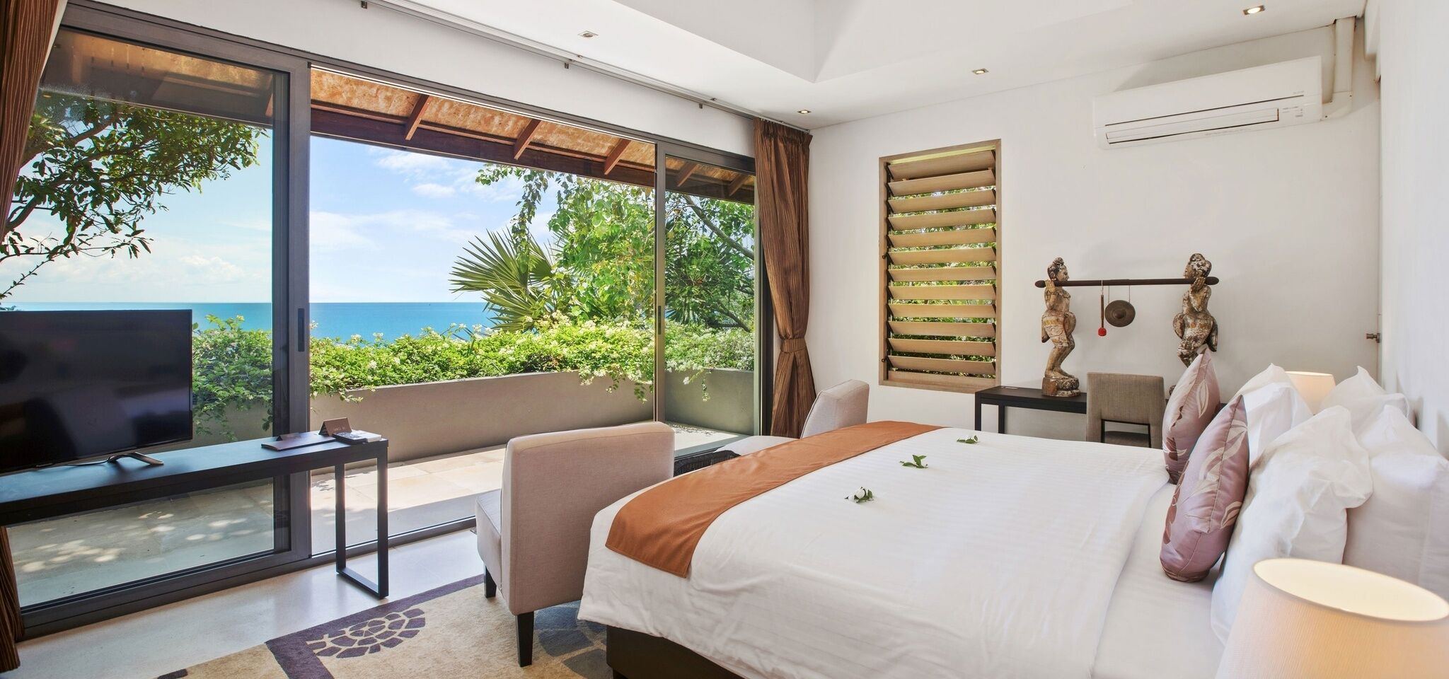 A modern hotel room with a large bed, a TV, a desk, and a view of the ocean.
