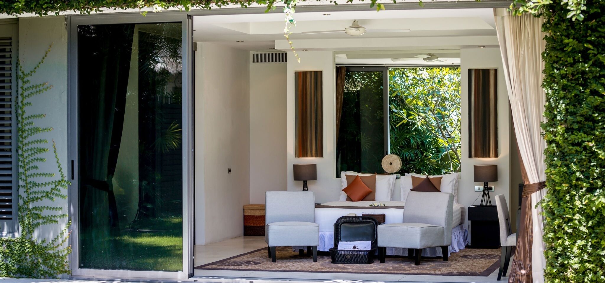 A modern room with a glass door leading to a garden, a sofa set, and a small table with lamps.