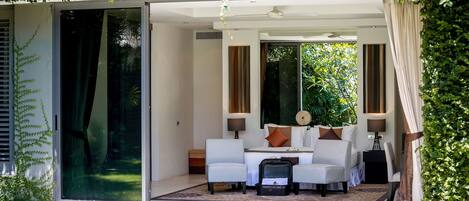 A modern room with a glass door leading to a garden, a sofa set, and a small table with lamps.