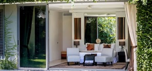 Una stanza moderna con una porta in vetro che dà su un giardino, una zona con divano e un piccolo tavolo con lampade.