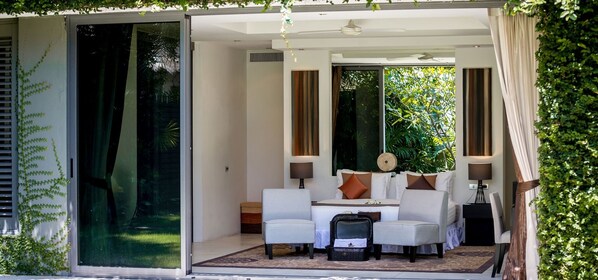 A modern room with a glass door leading to a garden, a sofa set, and a small table with lamps.