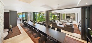 Un'area pranzo moderna con un tavolo lungo e sedie, un'accogliente zona relax con divani e ampie porte vetrate che si aprono su un giardino.