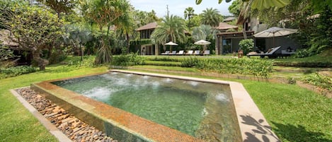 Una piscina rectangular con agua cristalina, rodeada por un borde de piedra y un lecho de guijarros.