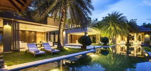 Una casa moderna con piscina, sillas de descanso y palmeras.