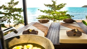 A beachside lounge with wooden flooring, two reclining beds with pillows and towels, a large bowl of fruit, and a view of the ocean. - Sangsuri Villa 3 (Koh Samui)