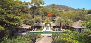 Un resort con varias cabañas de techo de paja, una piscina central y abundante vegetación.