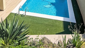 A rectangular swimming pool with a clear blue water surface, surrounded by a well-maintained lawn and a stone wall.