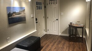 A hallway with a wooden floor, a white door, a bench, a table with items, and a wall-mounted picture. - Pet friendly Bungalow. Close to Downtown and Mountains! (Lakewood)