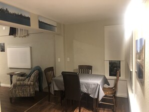 A dining area with a table set for four, surrounded by chairs. There is a window with blinds, a radiator, and a wall-mounted picture frame. - Pet friendly Bungalow. Close to Downtown and Mountains! (Lakewood)