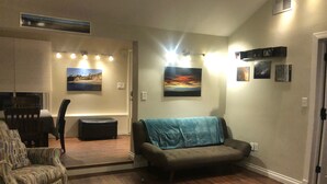 A living room with a sofa, armchair, and a wooden coffee table. There are wall-mounted lights and framed pictures on the walls. - Pet friendly Bungalow. Close to Downtown and Mountains! (Lakewood)