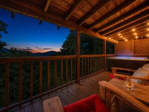 Une terrasse en bois avec un jacuzzi, des sièges et une vue sur les montagnes au crépuscule.
