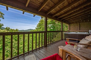 A wooden deck with a hot tub, seating area, and a view of the surrounding forest. - Cabin with Amazing View near Nat’l Park (Sevierville)