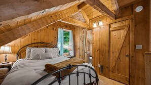 Une chambre à coucher dans une cabane en bois, avec un lit, une table de chevet, une lampe et une fenêtre avec des rideaux.