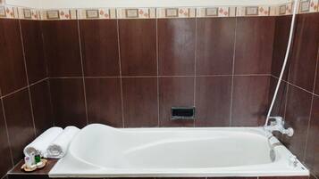 A bathtub with a showerhead, a towel, and a bottle on a tray.