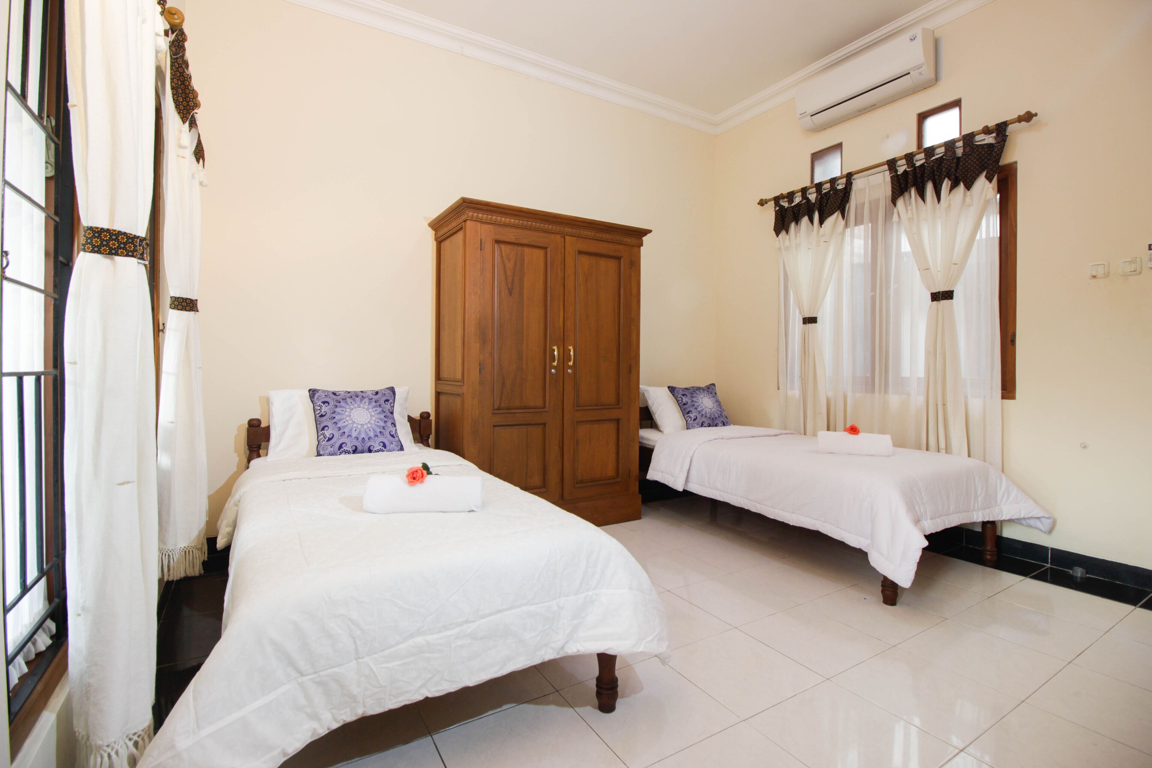 A hotel room with two beds, a wooden wardrobe, and a window with curtains.