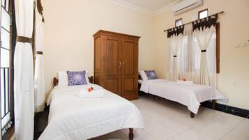 A hotel room with two beds, a wooden wardrobe, and a window with curtains.