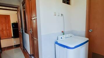 A hallway with a washing machine, a small basket, and a door.