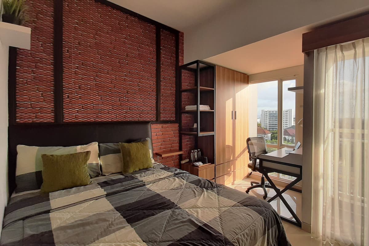 A modern bedroom with a large bed, a desk, and a city view through the window.