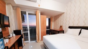 Een hotelkamer met een bed, een bureau, een stoel, een televisie en een balkon met gordijnen.