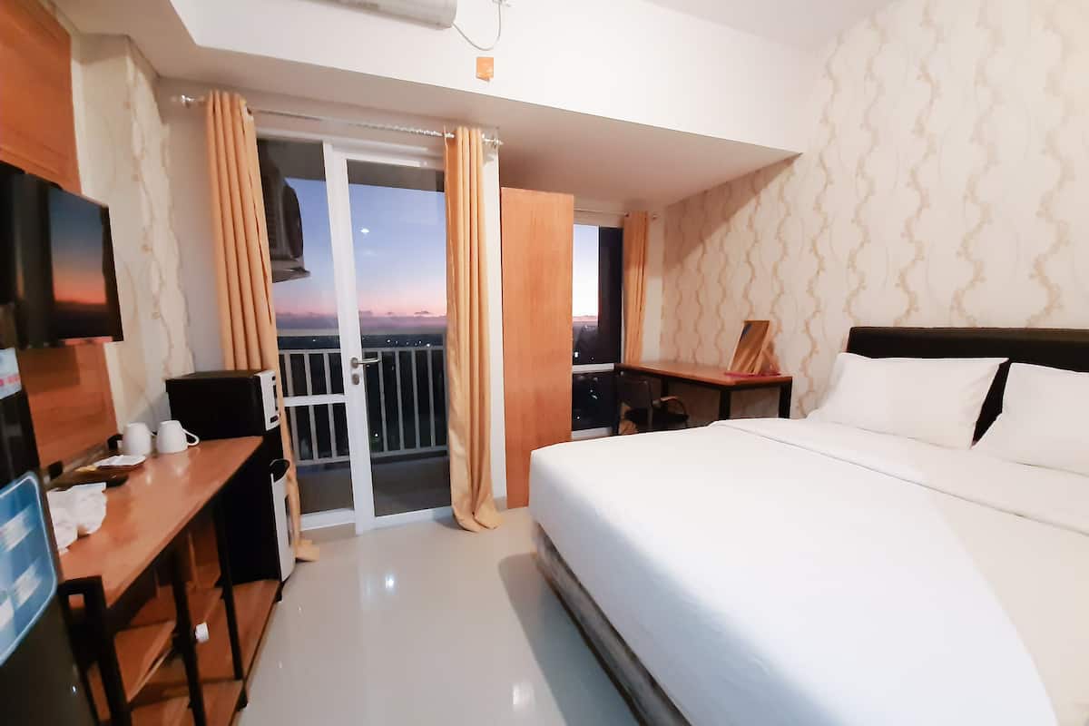 A hotel room with a bed, a desk, a chair, a TV, and a balcony with curtains.