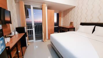 A hotel room with a bed, a desk, a chair, a TV, and a balcony with curtains.
