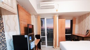 Een compacte hotelkamer met een kitchenette, een bed en een balkon met gordijnen.