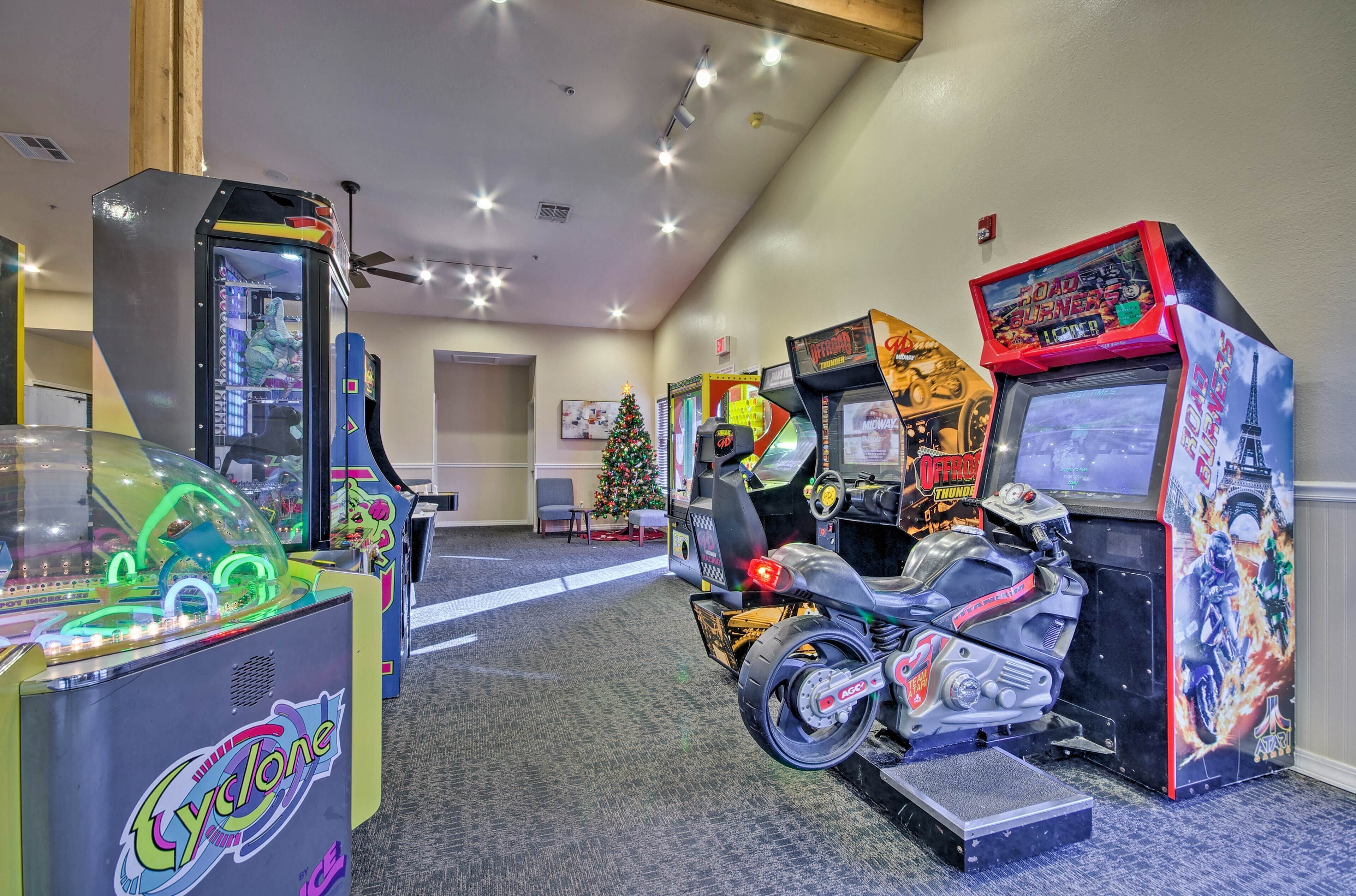 A row of arcade machines, including 'Cyclone' and 'Road Bumpers', in a room with a Christmas tree and a motorcycle.