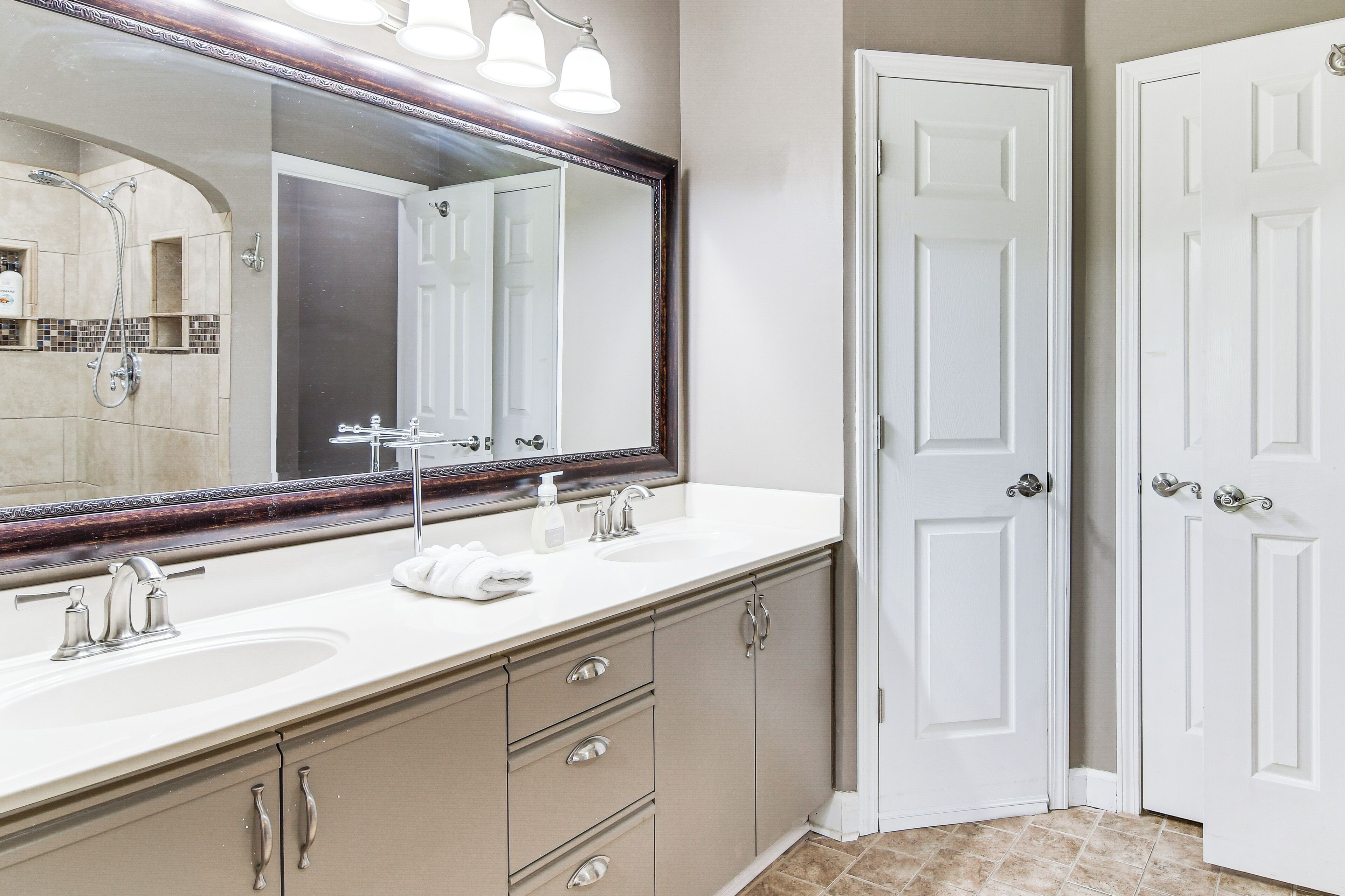 A bathroom with a large mirror, two sinks, a shower, and a door.