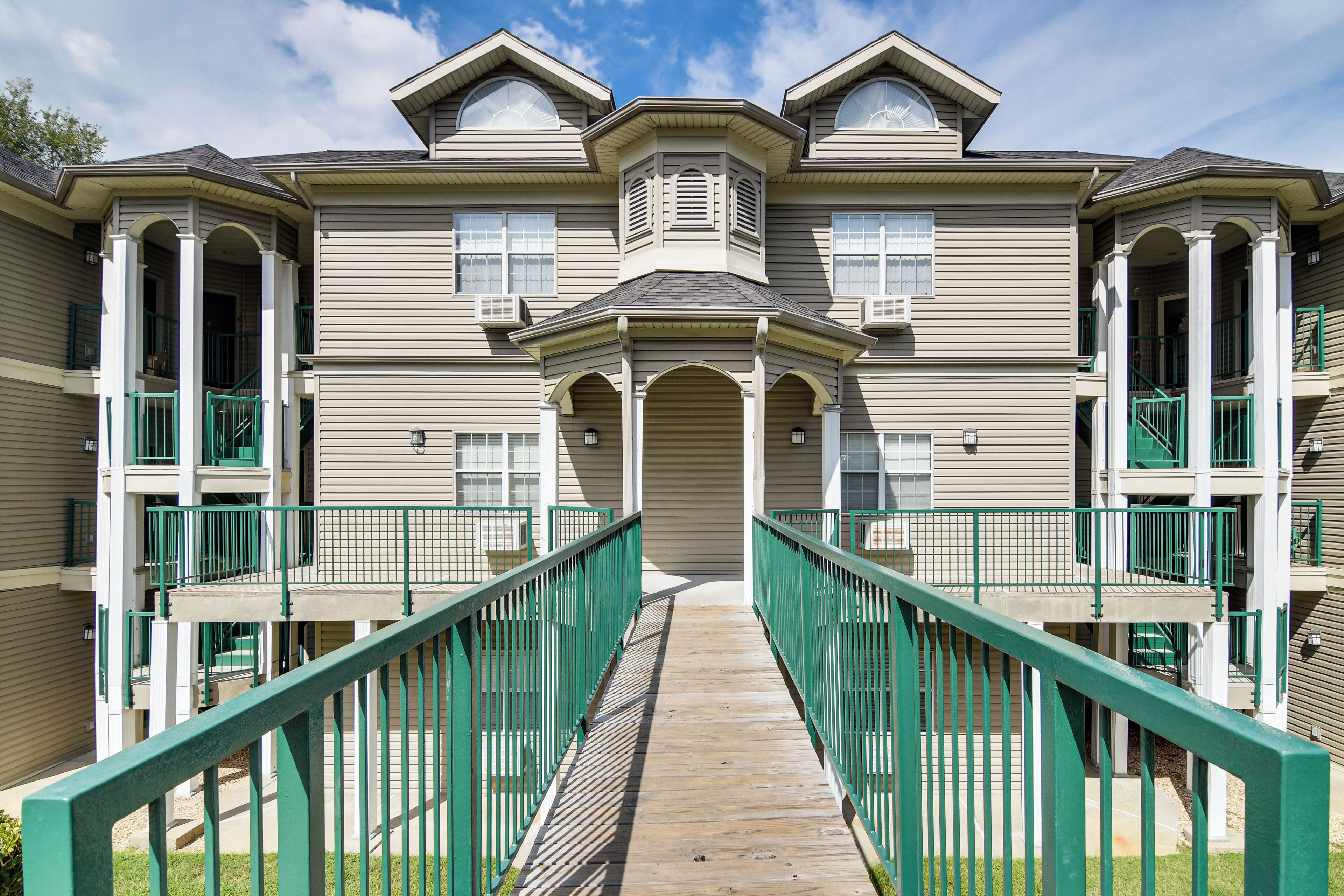 A multi-story building with a central entrance, green railings, and a symmetrical facade.